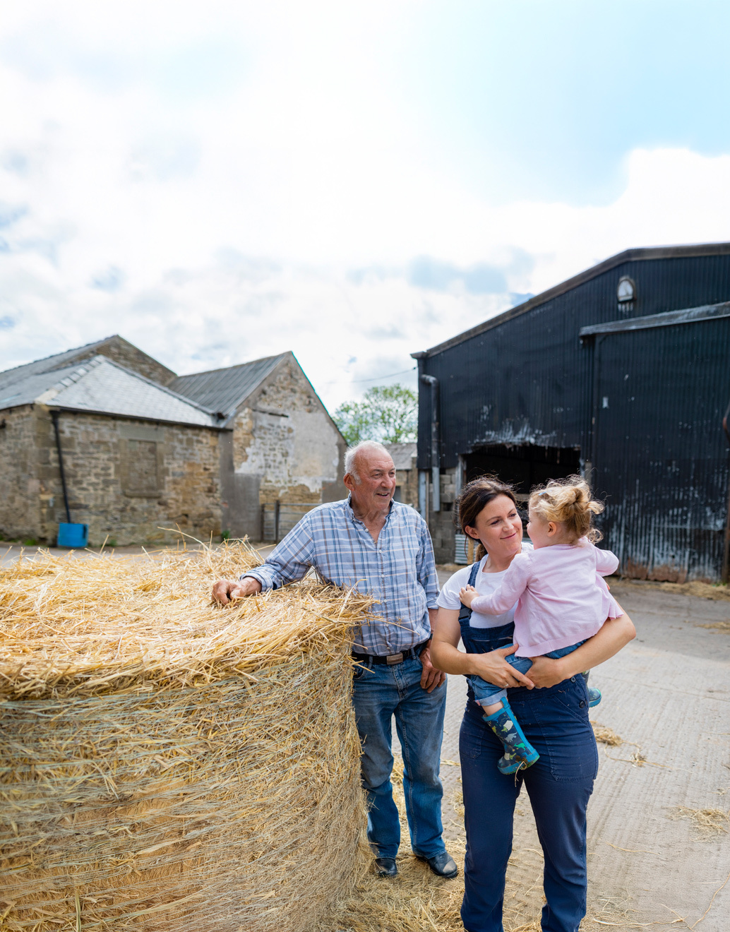 Mother holding her daughter and standing with a senior man on a farm