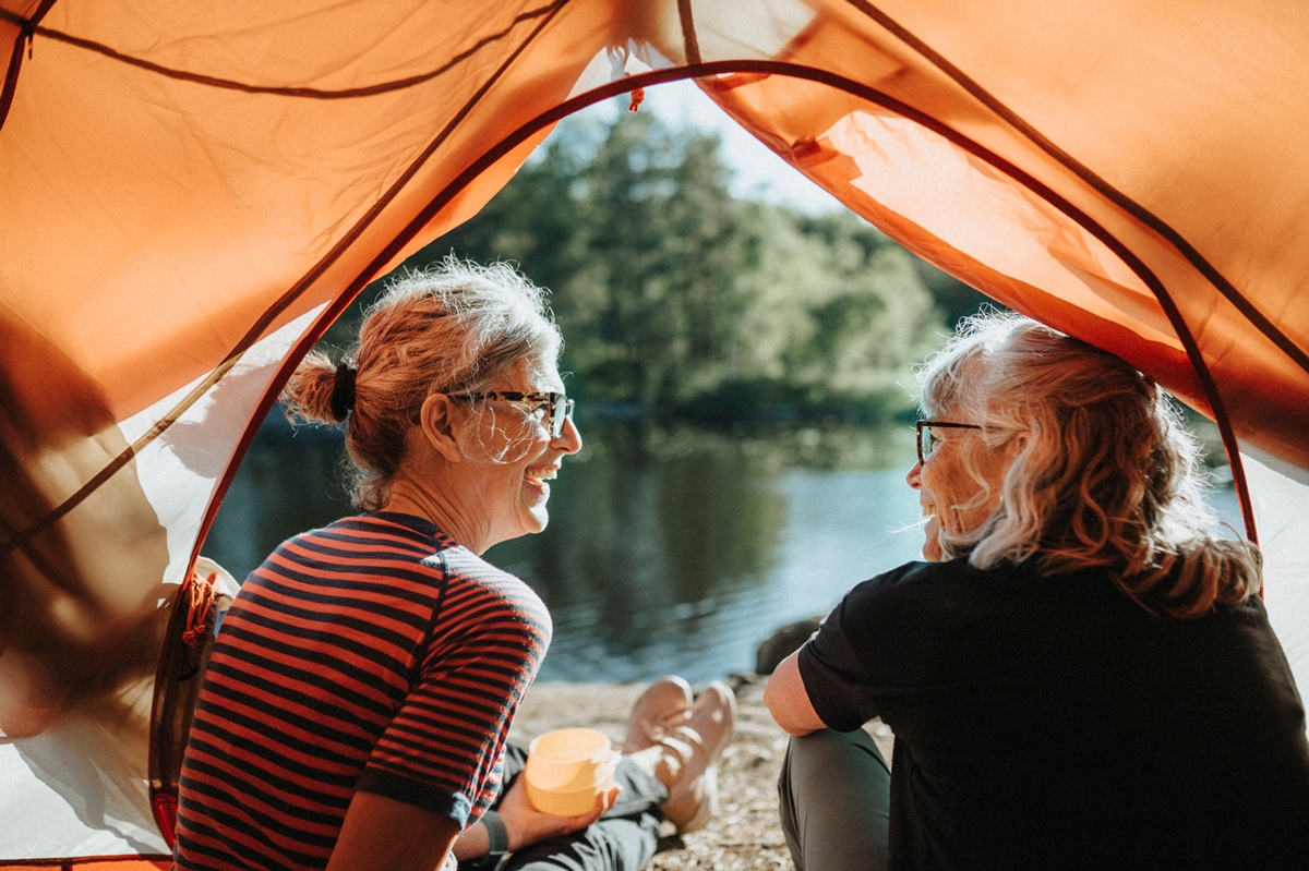Two women sitting in a tent by a lake